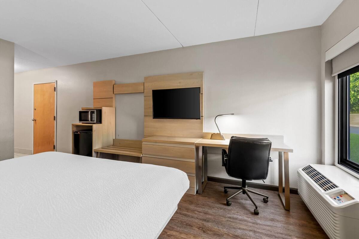 Una habitación de hotel con cama, escritorio con silla, televisor, microondas y ventana.