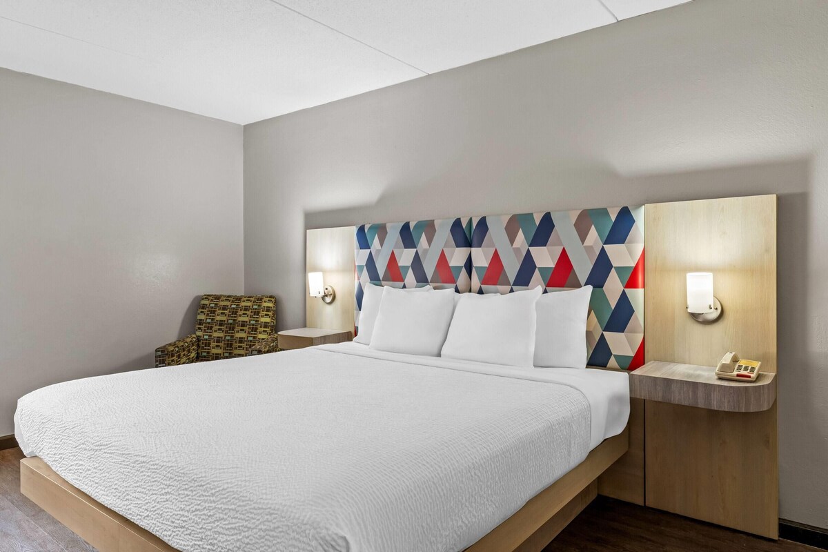Habitación de hotel con una cama grande, dos mesitas de noche, una silla y un cabecero con diseño geométrico.