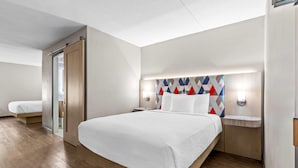 A modern hotel room with a large bed, a wooden floor, a glass door, and a geometric-patterned headboard. - Days Inn & Suites by Wyndham Peachtree Corners/Norcross (Peachtree Corners)