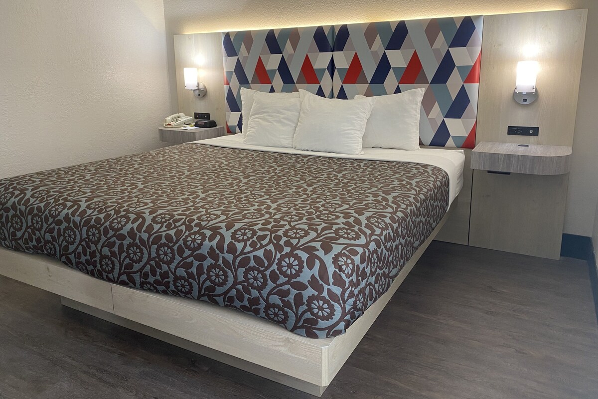 Una habitación de hotel moderna con una cama grande, una mesita de noche con lámpara y un cabecero de diseño geométrico.