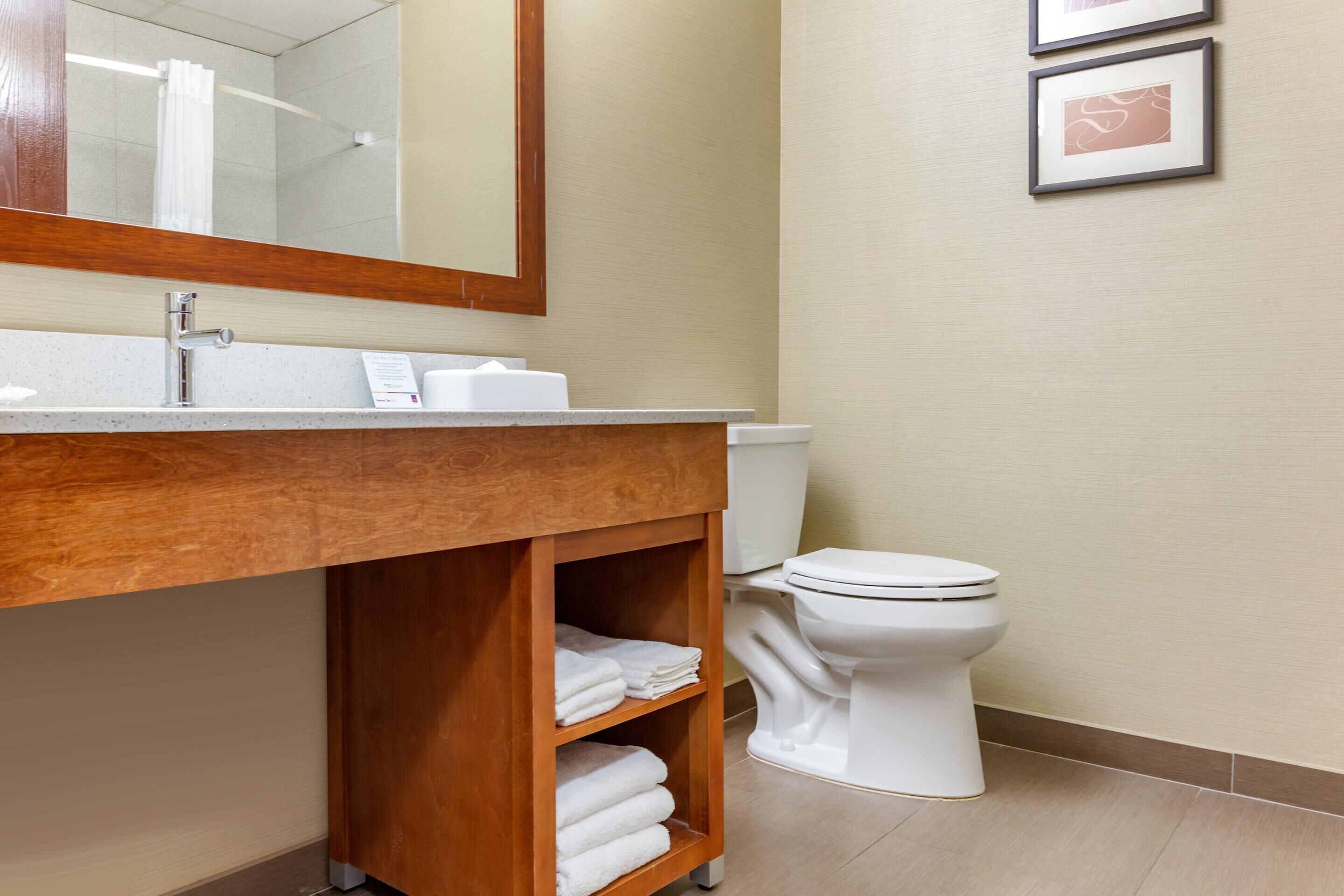 A bathroom with a wooden vanity, a white toilet, and a mirror above the sink.