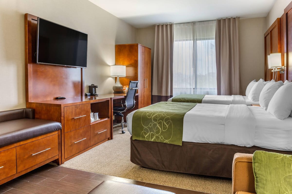 A hotel room with a bed, a desk, a chair, a TV, and a window with curtains.