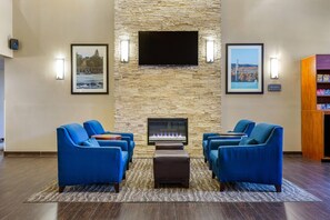 A lobby with a stone wall, a flat-screen TV, framed pictures, blue sofas, a fireplace, and a wooden bookshelf. - Comfort Suites Dover University Area (Dover)
