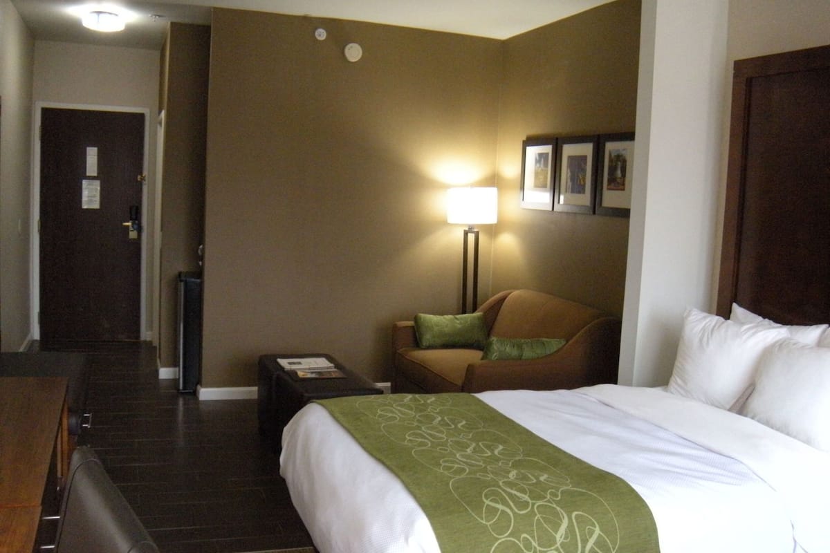 A hotel room with a bed, a chair, a desk, and a lamp.