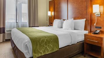 A hotel room with a large bed, a wooden headboard, two bedside lamps, a telephone, and a window with curtains.