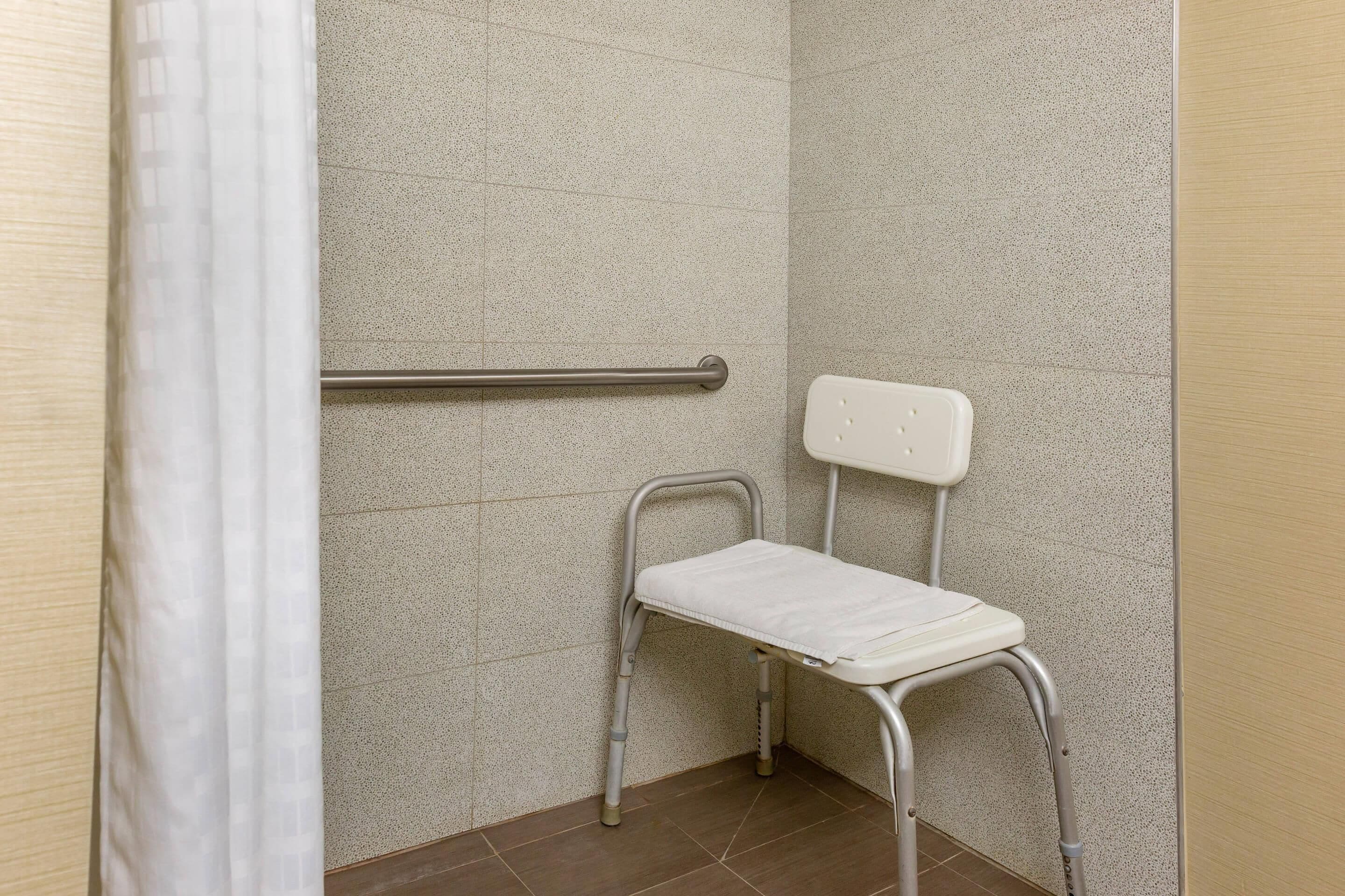 Un baño con cortina de ducha blanca, barra de apoyo y un inodoro portátil blanco.