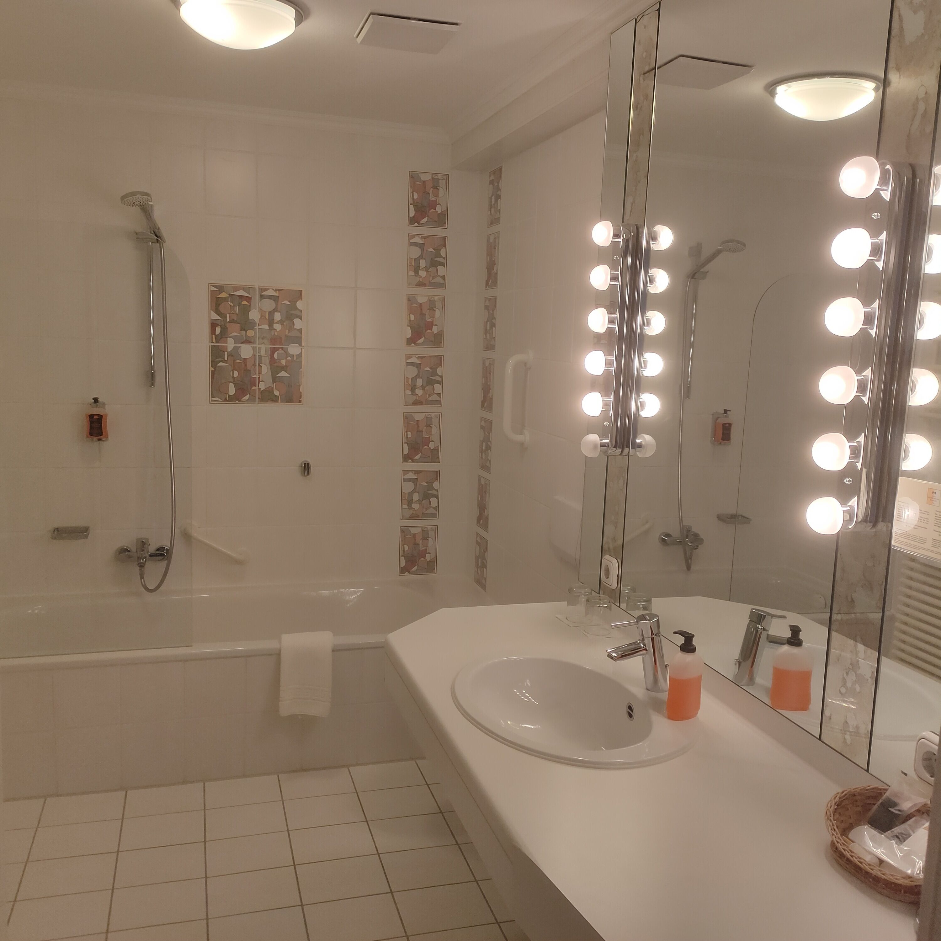 A modern bathroom with a bathtub, a large mirror with lights, and a sink.