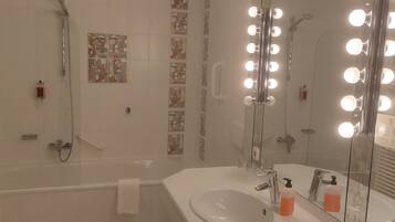 A modern bathroom with a bathtub, a large mirror with lights, and a sink.