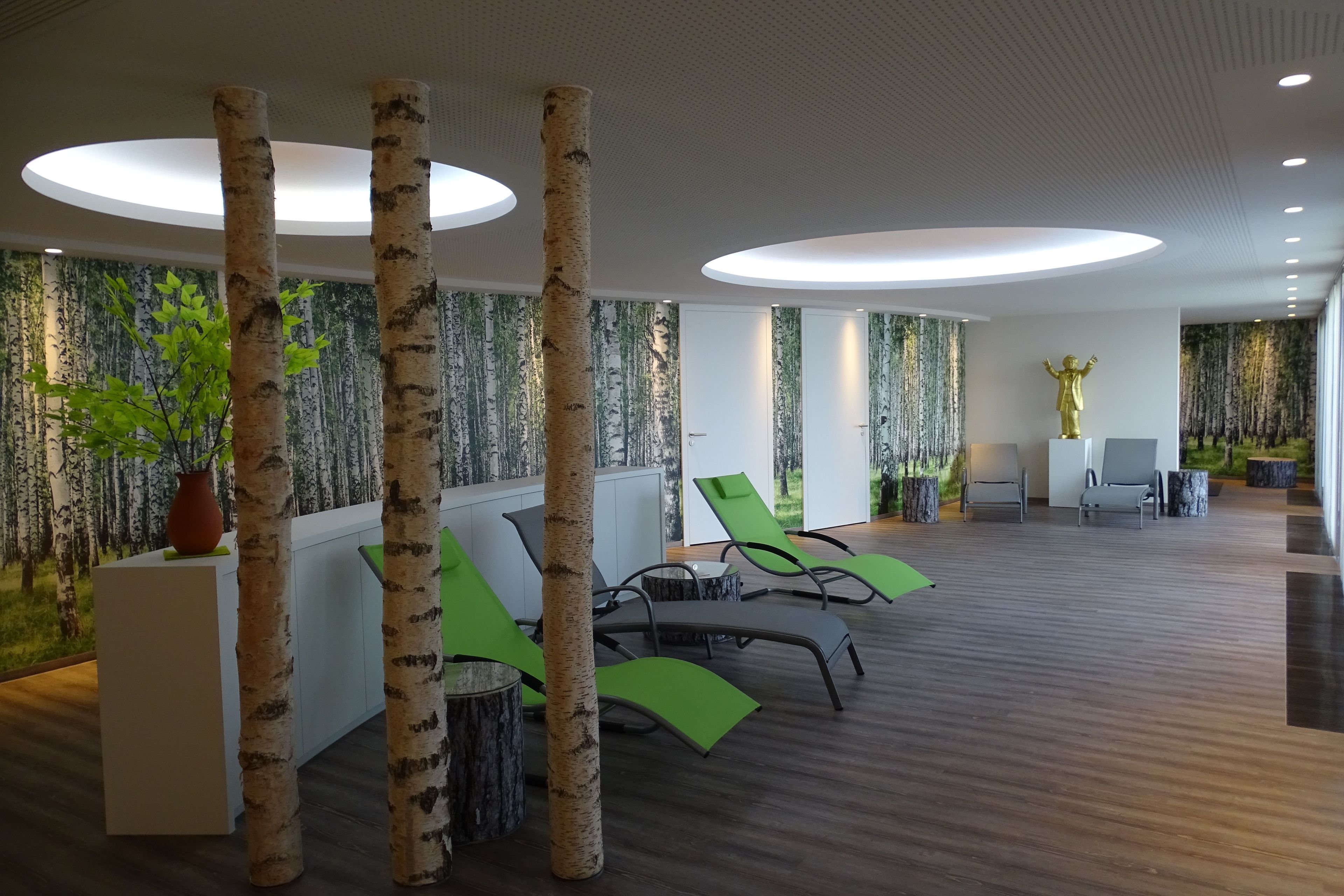 A modern indoor space with birch tree columns, green lounge chairs, and a large golden statue.