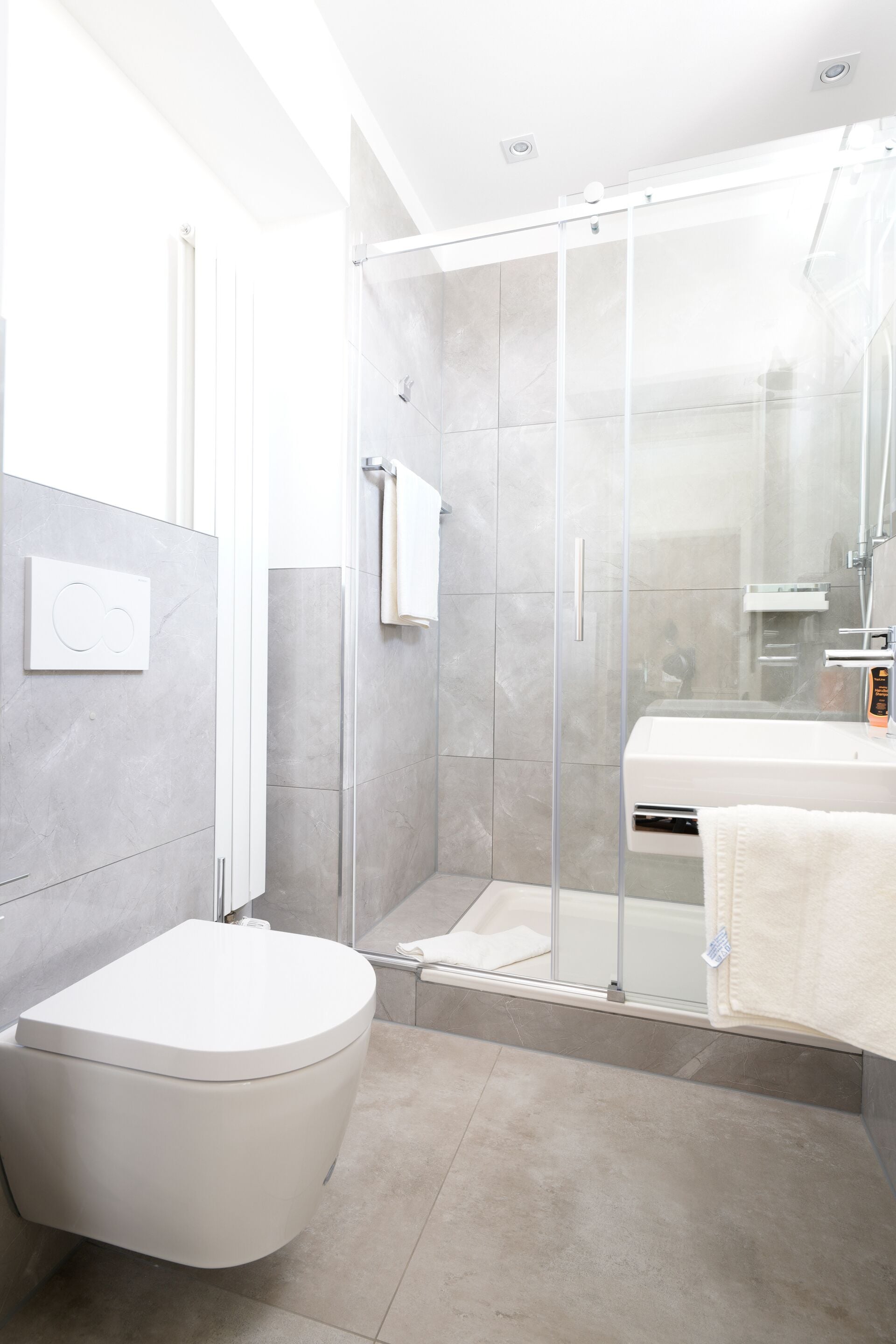 Un baño moderno con inodoro, ducha con mampara de vidrio y lavabo con espejo.