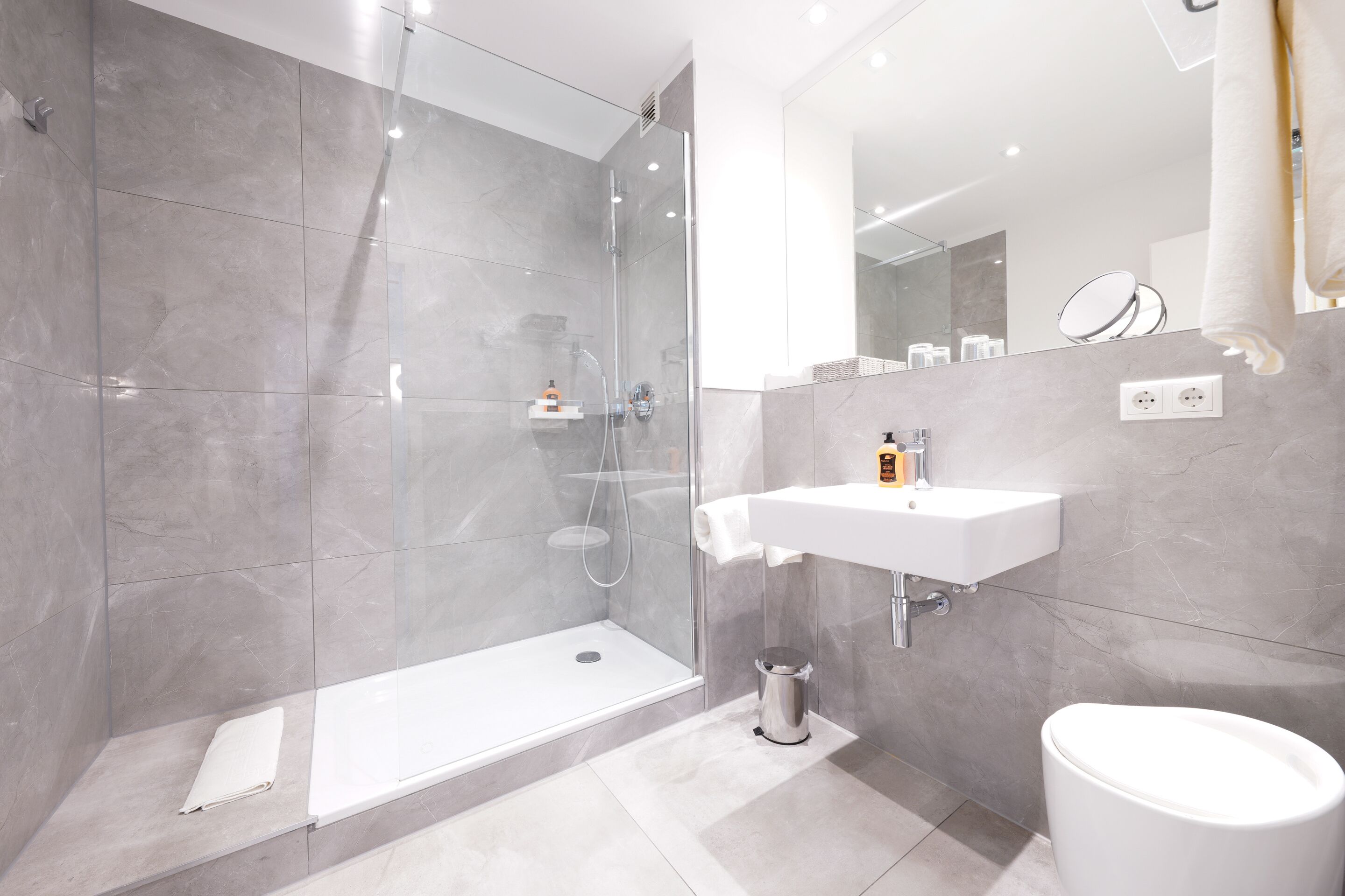A modern bathroom with a glass-enclosed shower, a white sink, and a toilet.