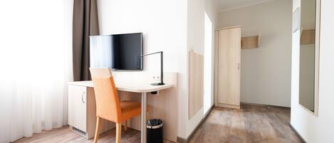 A modern hotel room with a desk, chair, TV, and a small trash bin.