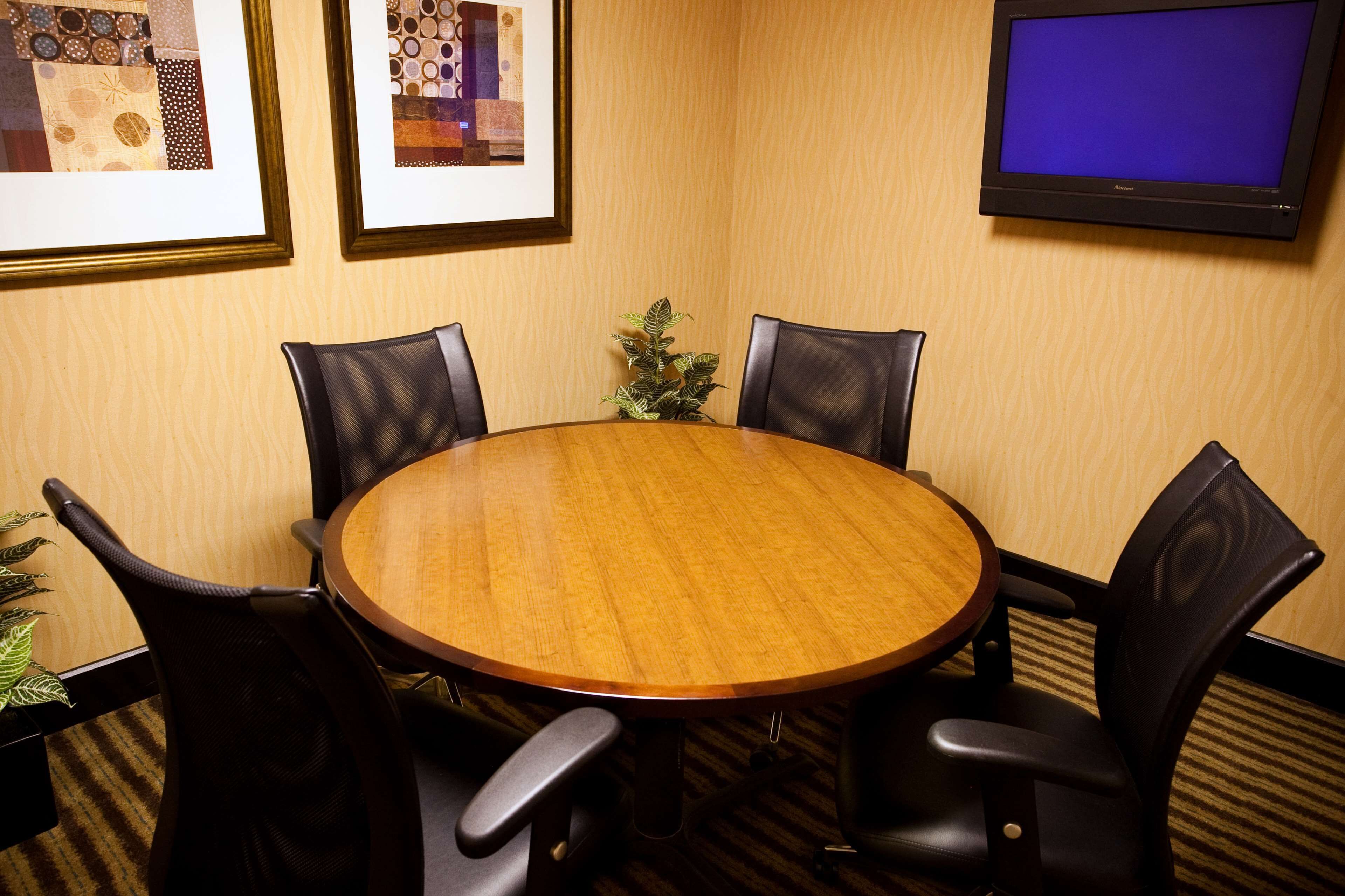 A conference room with a wooden table, black leather chairs, framed artwork on the wall, and a flat-screen TV.