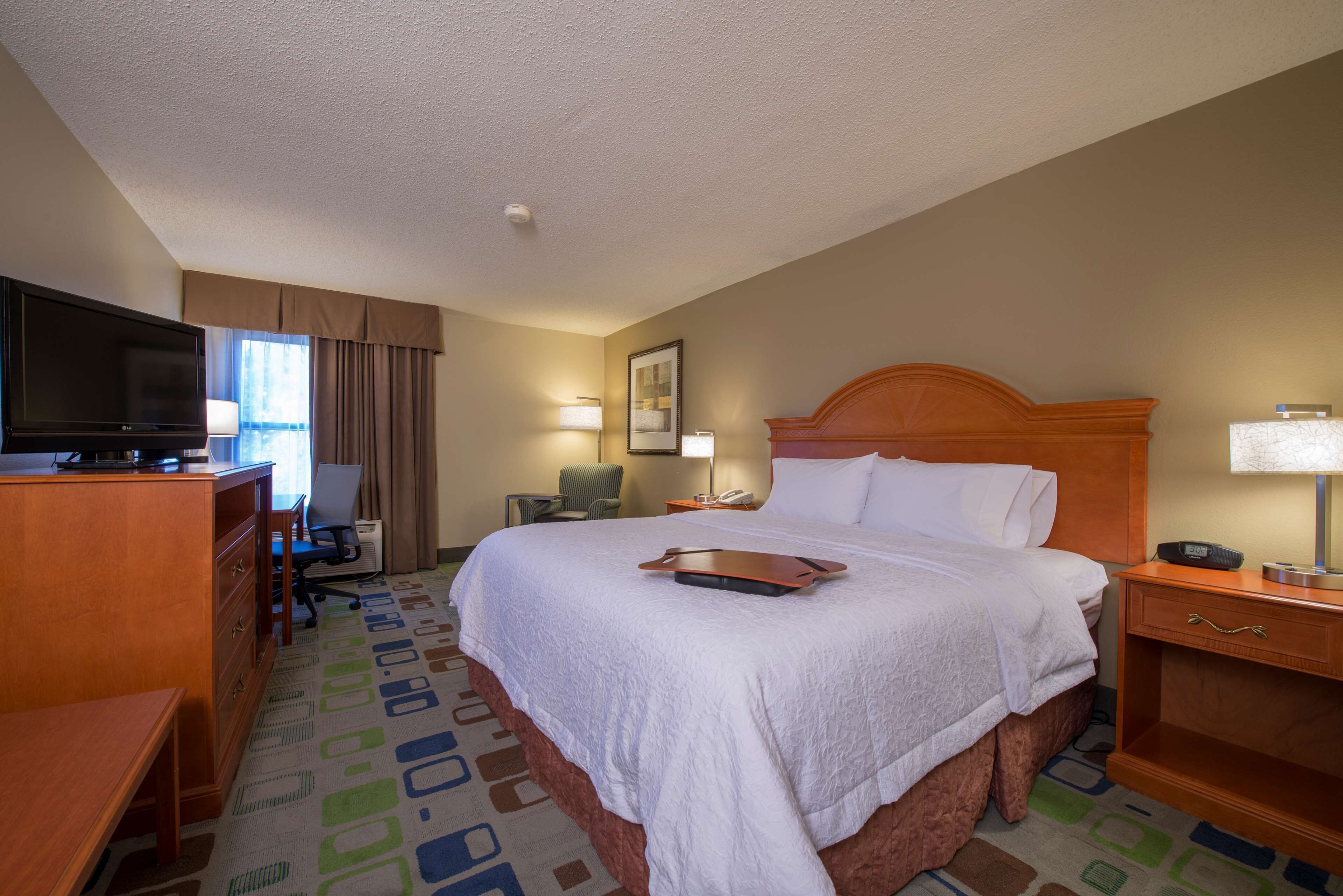 Una habitación de hotel con una cama grande, un escritorio con televisor, una silla y una lámpara.