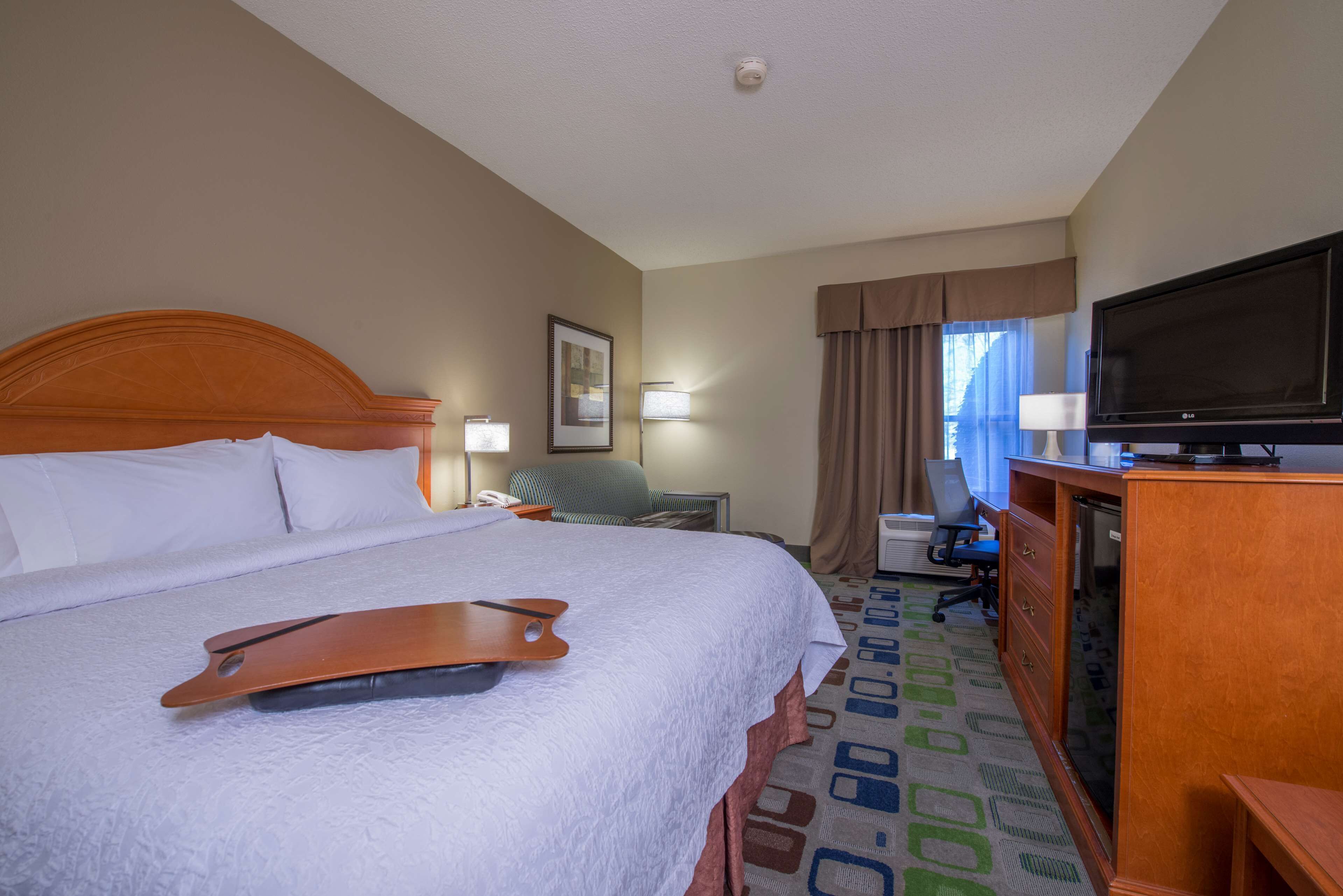 Una habitación de hotel con una cama grande, un escritorio con computadora, un televisor y una silla.