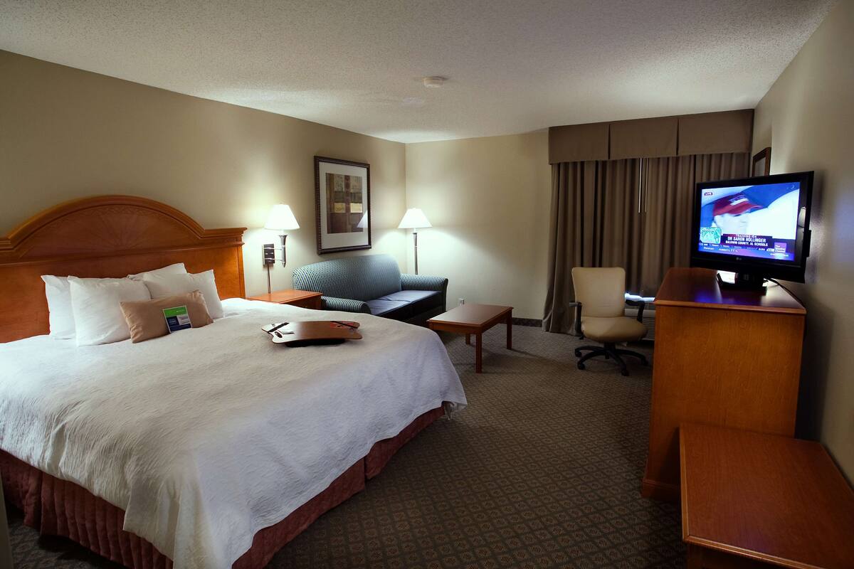 A hotel room with a large bed, a desk with a computer, a television, and a chair.