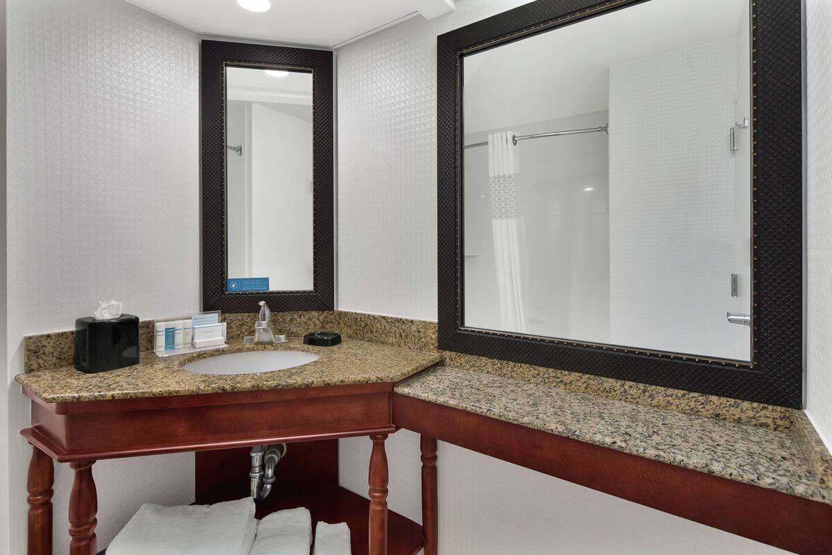 A bathroom with a granite countertop sink, a wooden vanity, and two mirrors.