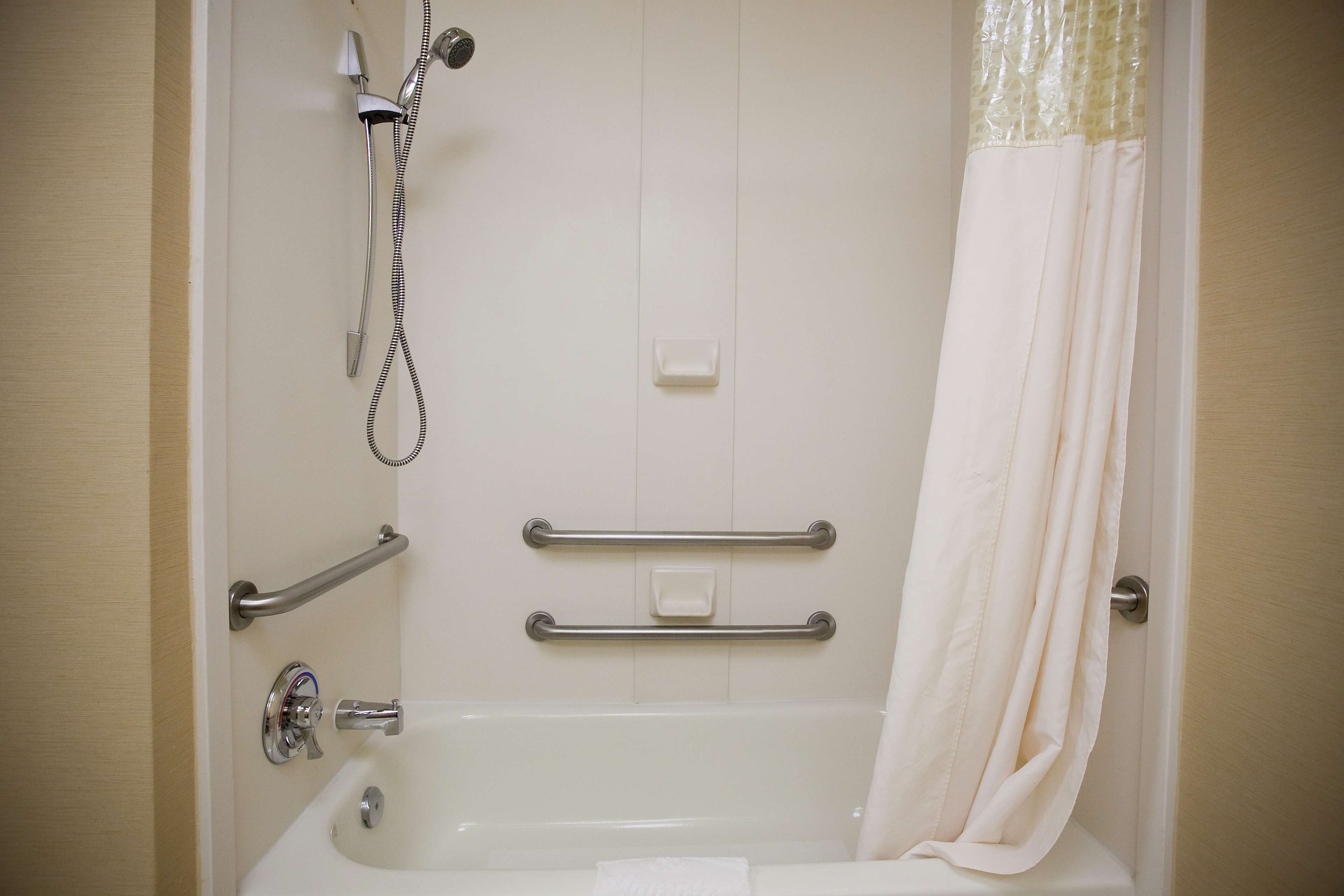 A bathroom with a bathtub, grab bars, a showerhead, and a curtain.