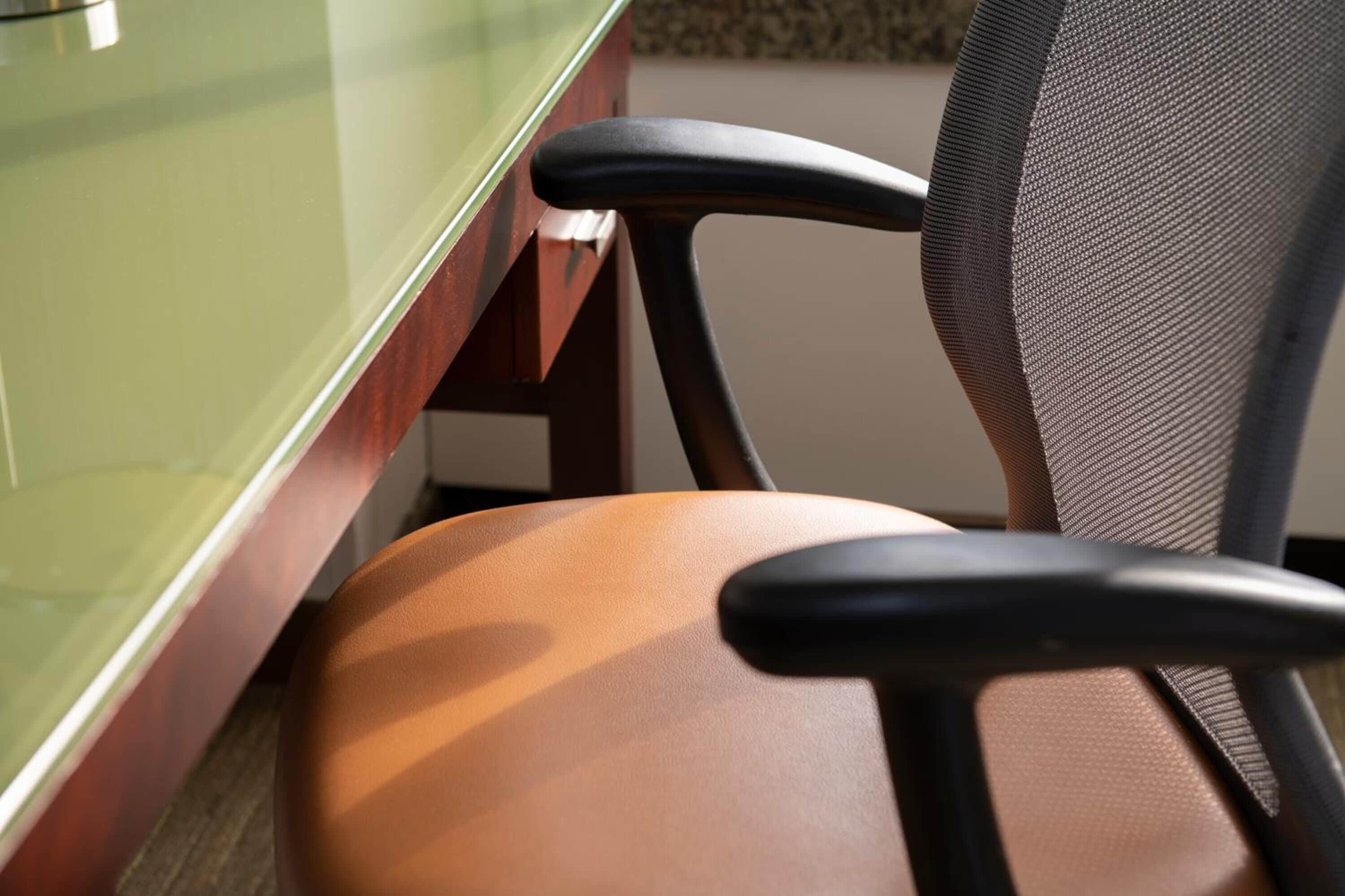 A close-up of a chair with a mesh backrest and a cushioned seat, positioned next to a glass partition.