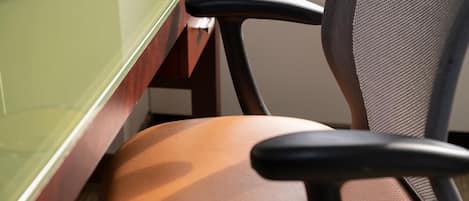 A close-up of a chair with a mesh backrest and a cushioned seat, positioned next to a glass partition.