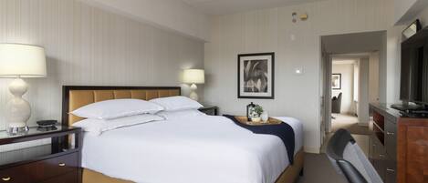 A hotel room with a bed, bedside lamps, a desk, a chair, a television, and a framed picture on the wall.