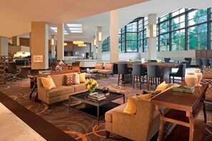 En rymlig hotellobby med modern design, som erbjuder en blandning av sittgrupper, en matplats och utsikt genom stora fönster.