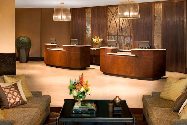 A reception area with two wooden reception desks, a coffee table with books and a vase of flowers, and a large potted plant.