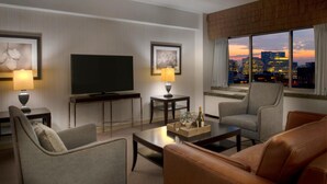 A hotel room with a city view, a flat-screen TV, two side tables with lamps, a sofa, and a coffee table.