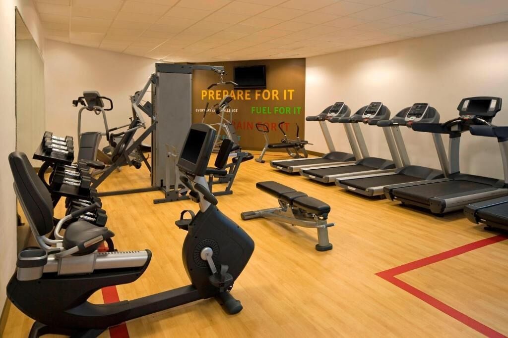 Un gimnasio con diverso equipo de ejercicio, incluyendo cintas de correr, elípticas y bancos de pesas.