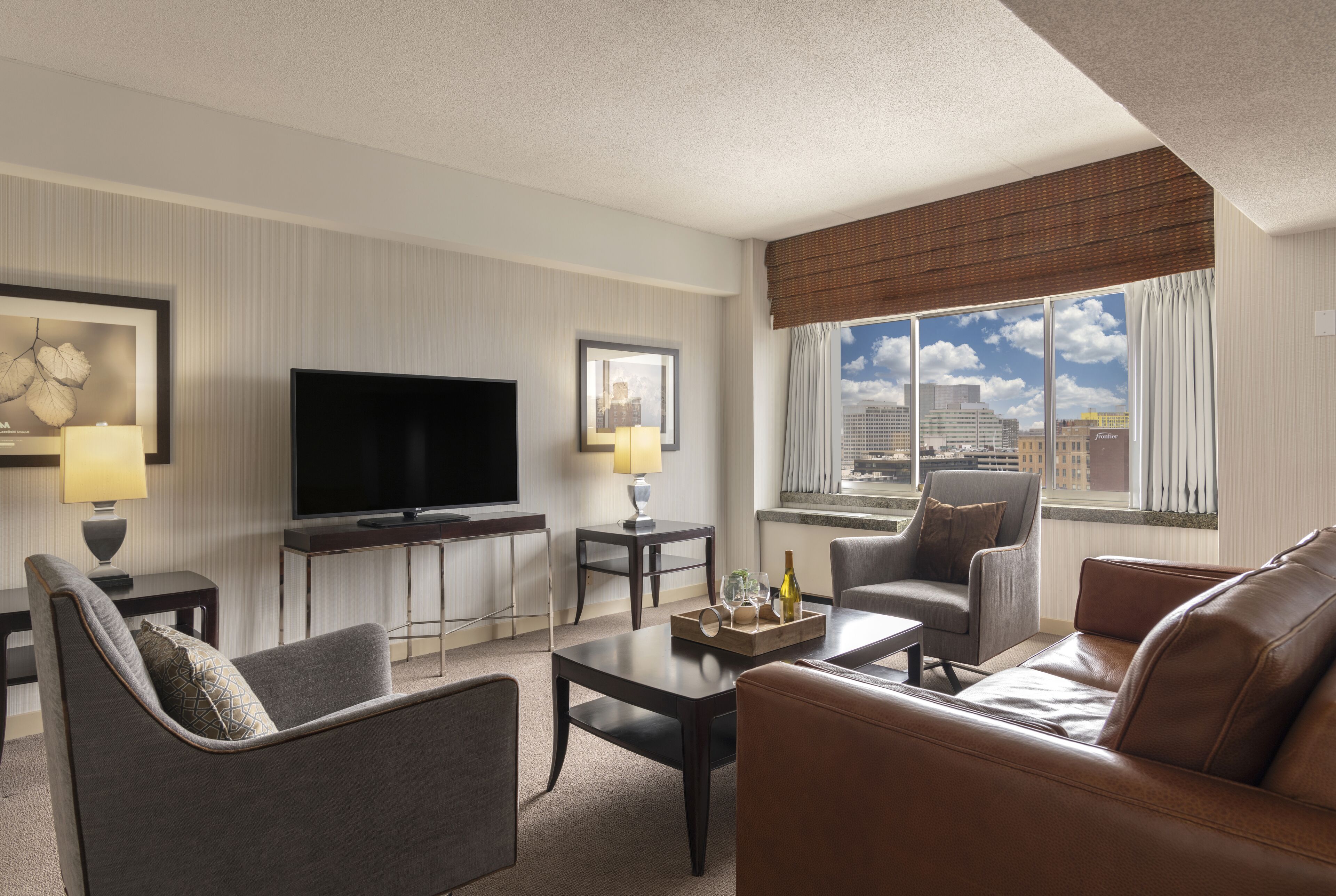 Une chambre d’h ôtel moderne équipée d’une télévision à écran plat, d’un canapé, d’un fauteuil, d’une table basse et d’une fenêtre donnant sur la ville.