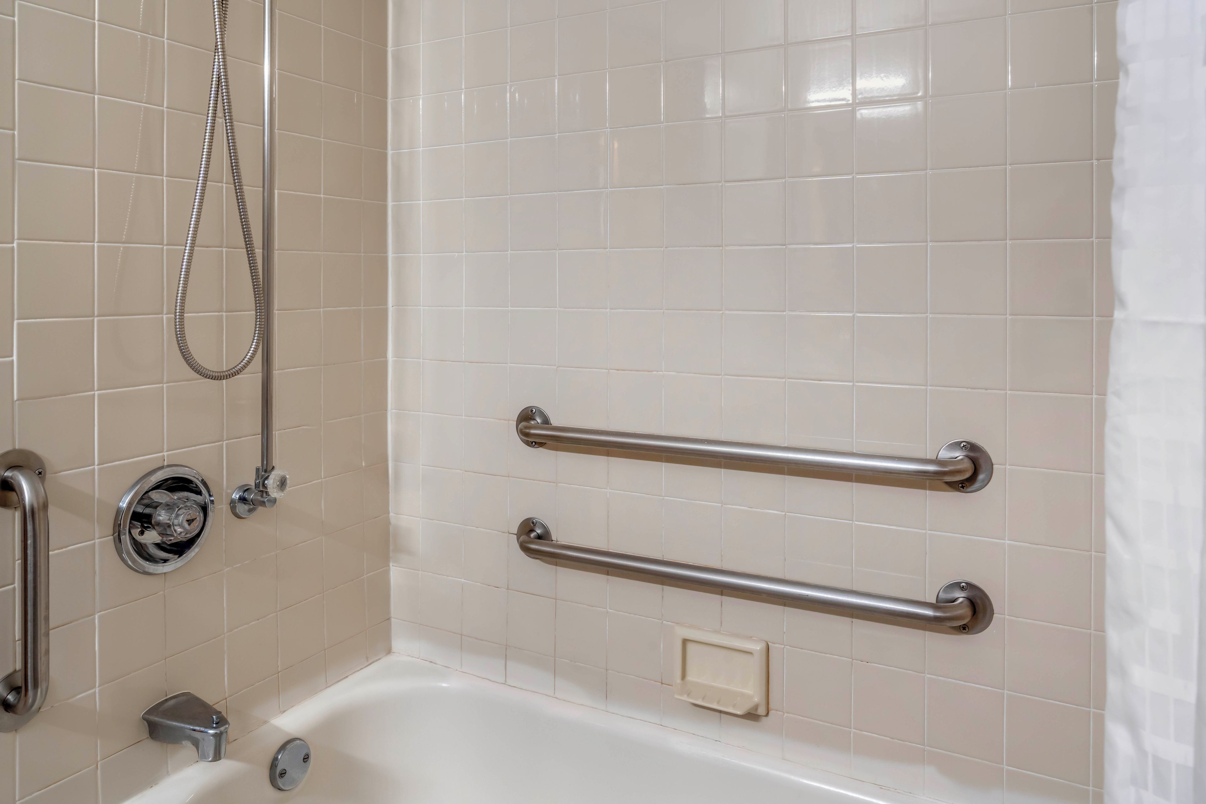 A bathroom with a bathtub, a shower, and grab bars for safety.