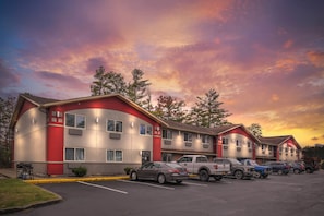 A motel with a curved facade, multiple windows, and a parking lot with several vehicles. - Red Roof Inn Queensbury (Queensbury)