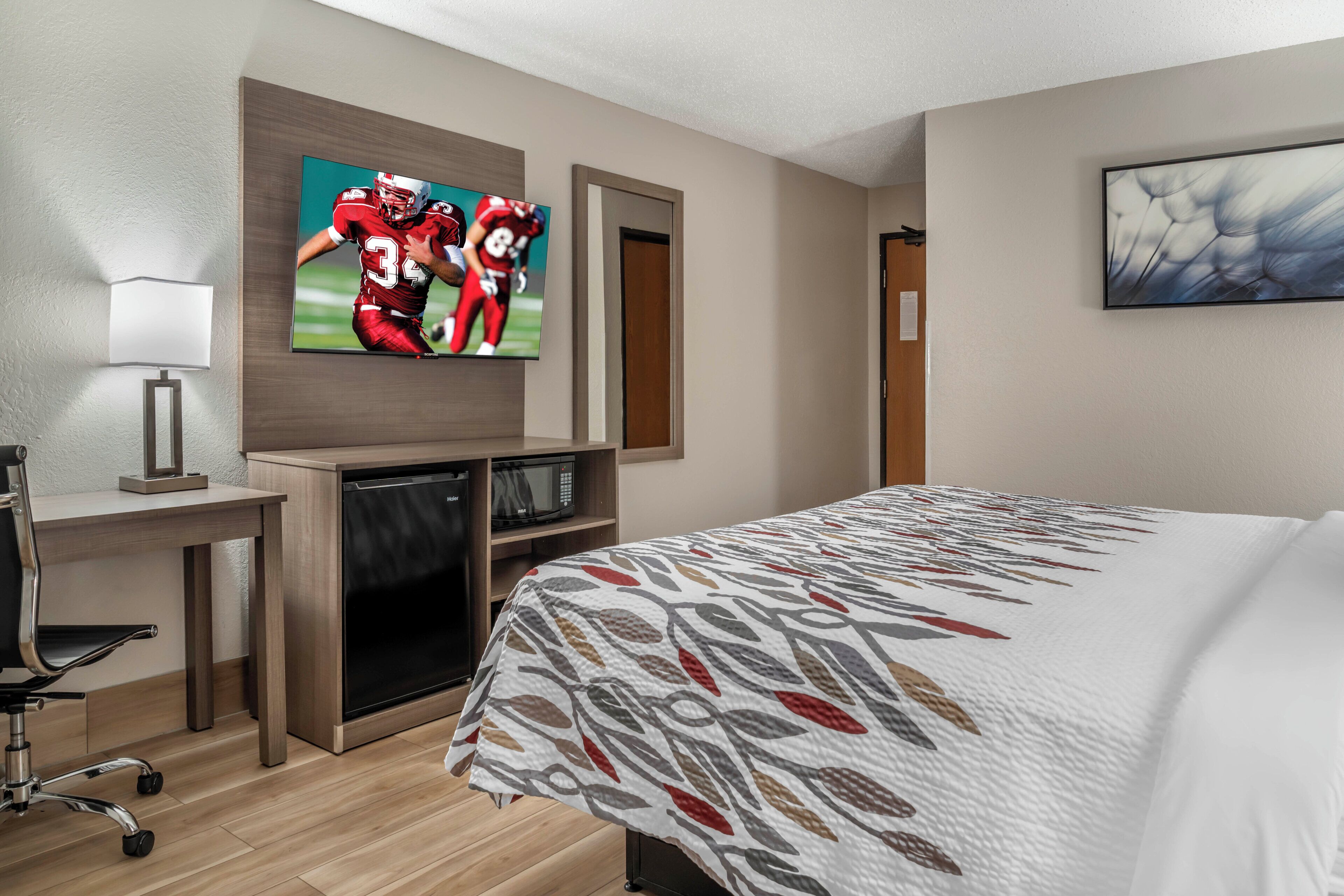 Habitación de hotel con cama, escritorio con lámpara, televisión, microondas y puerta.