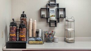 Estación de café con cafetera, tazas y un cartel con el horario de atención.