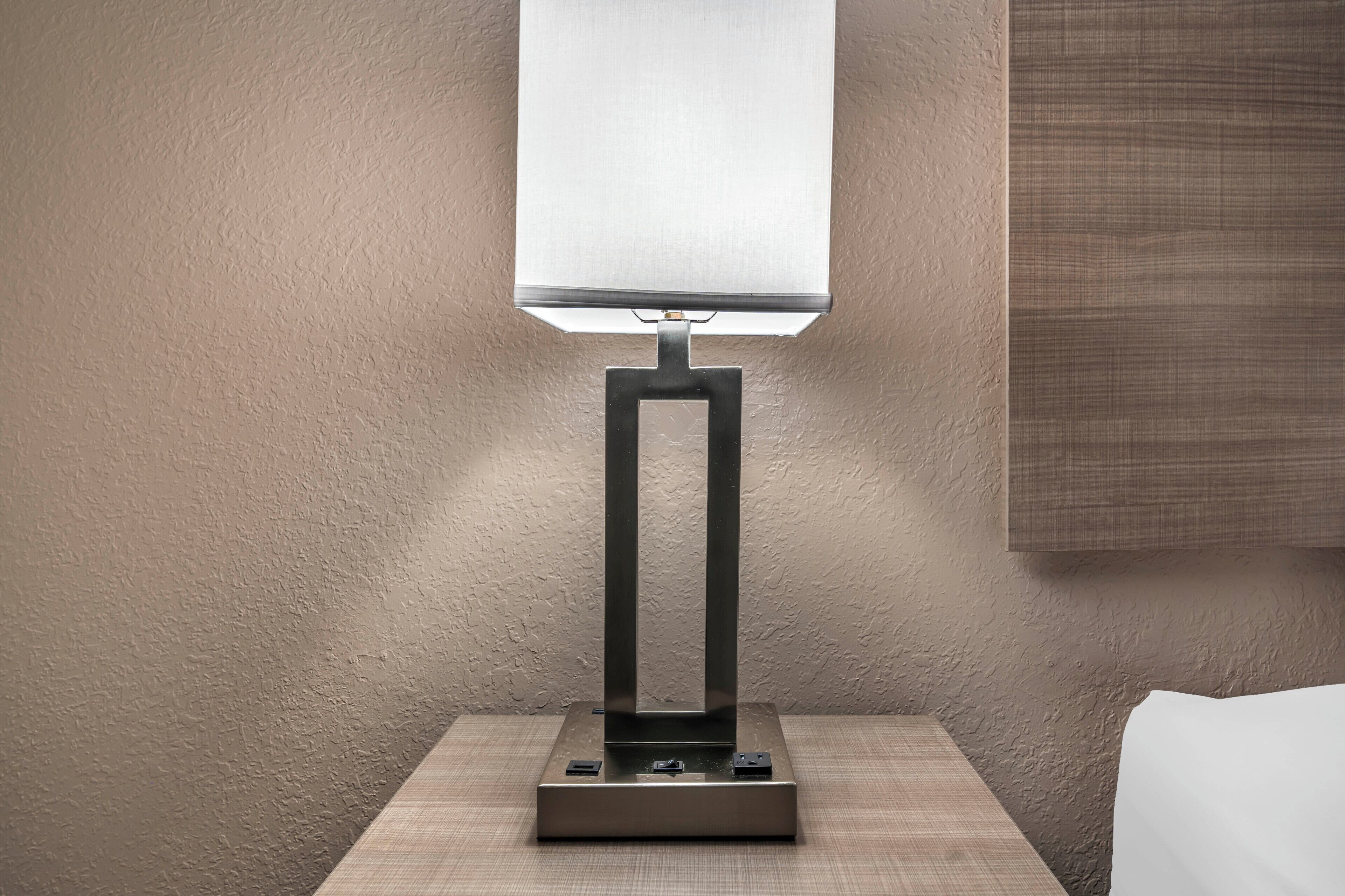 A modern table lamp with a rectangular base and a square lampshade on a wooden nightstand.