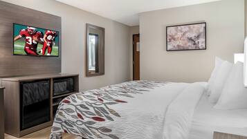 A hotel room with a bed, a television mounted on the wall, a microwave, and a door.