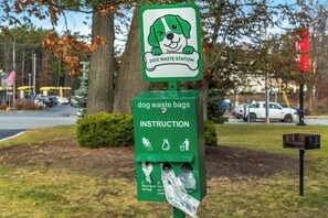 A dog waste station with a green sign and a cartoon dog illustration. - Red Roof Inn Queensbury (Queensbury)