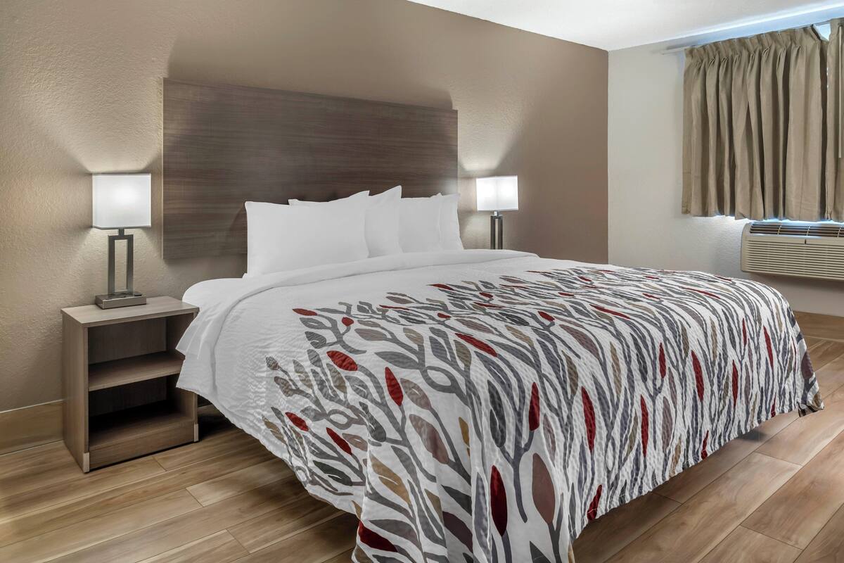 A neatly made bed with a patterned bedspread, two bedside tables with lamps, a wooden headboard, and a window with curtains.