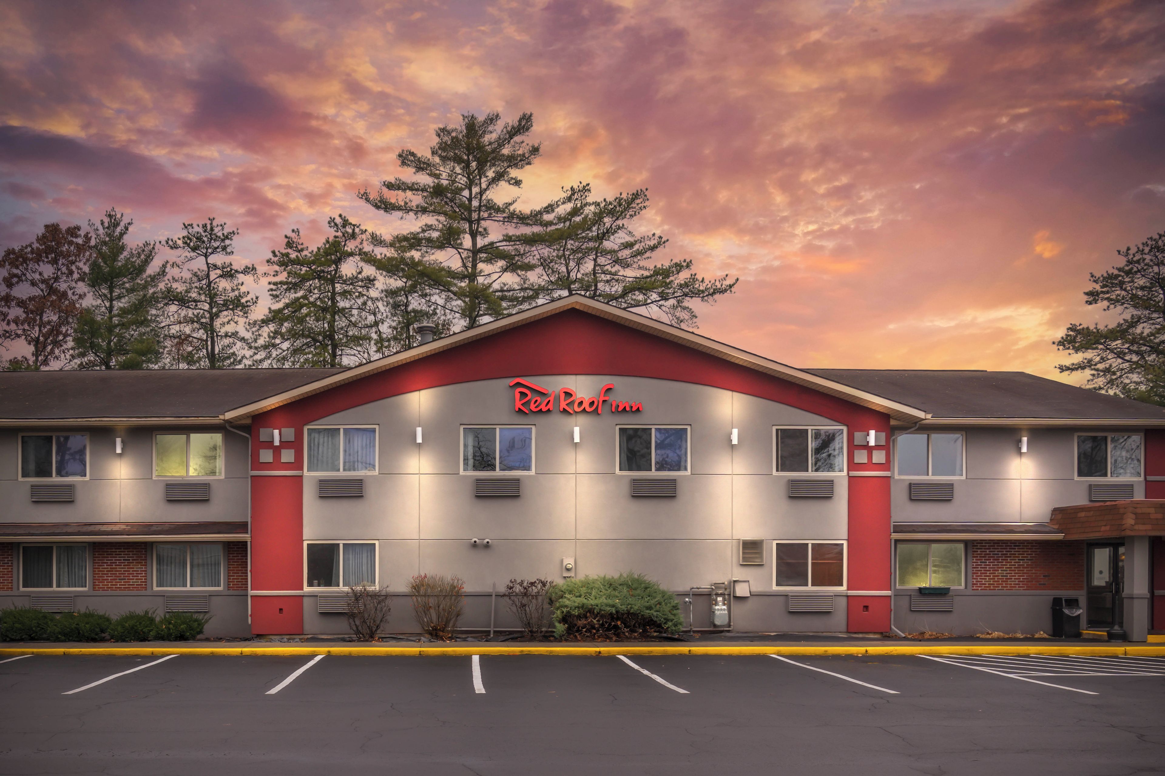 Un hôtel Red Roof Inn avec une façade rouge et grise, de nombreuses fenêtres et un parking situé à l’avant.