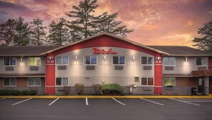Un hotel Red Roof Inn con fachada roja y gris, múltiples ventanas y un estacionamiento frente a él.