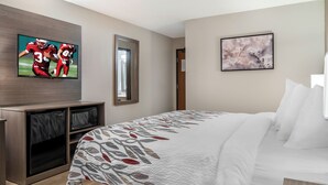 A hotel room with a bed, a TV mounted on the wall, a microwave, and a door. - Red Roof Inn Queensbury (Queensbury)