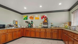 A kitchen with wooden cabinets, a microwave, a coffee machine, and various food items on the counter. - Quality Inn & Suites Morrow Atlanta South (Morrow)