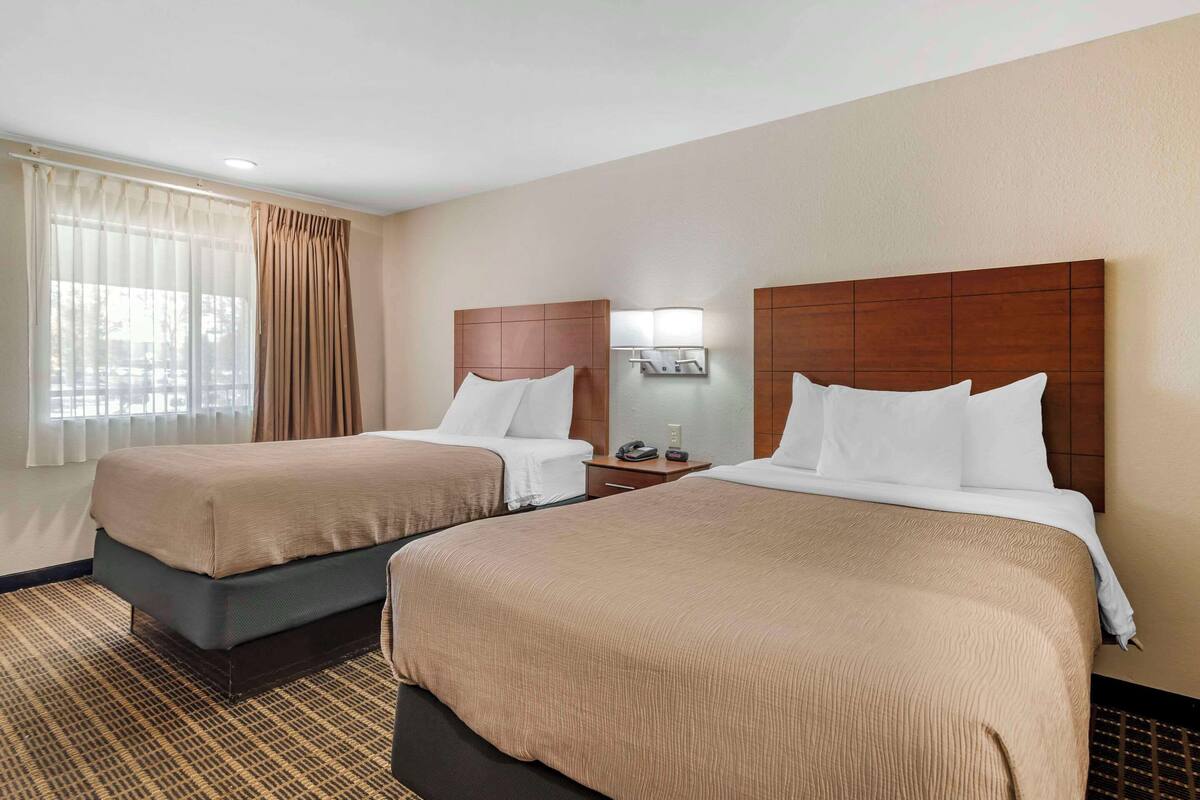 A hotel room with two beds, a nightstand with a lamp, and a window with curtains.
