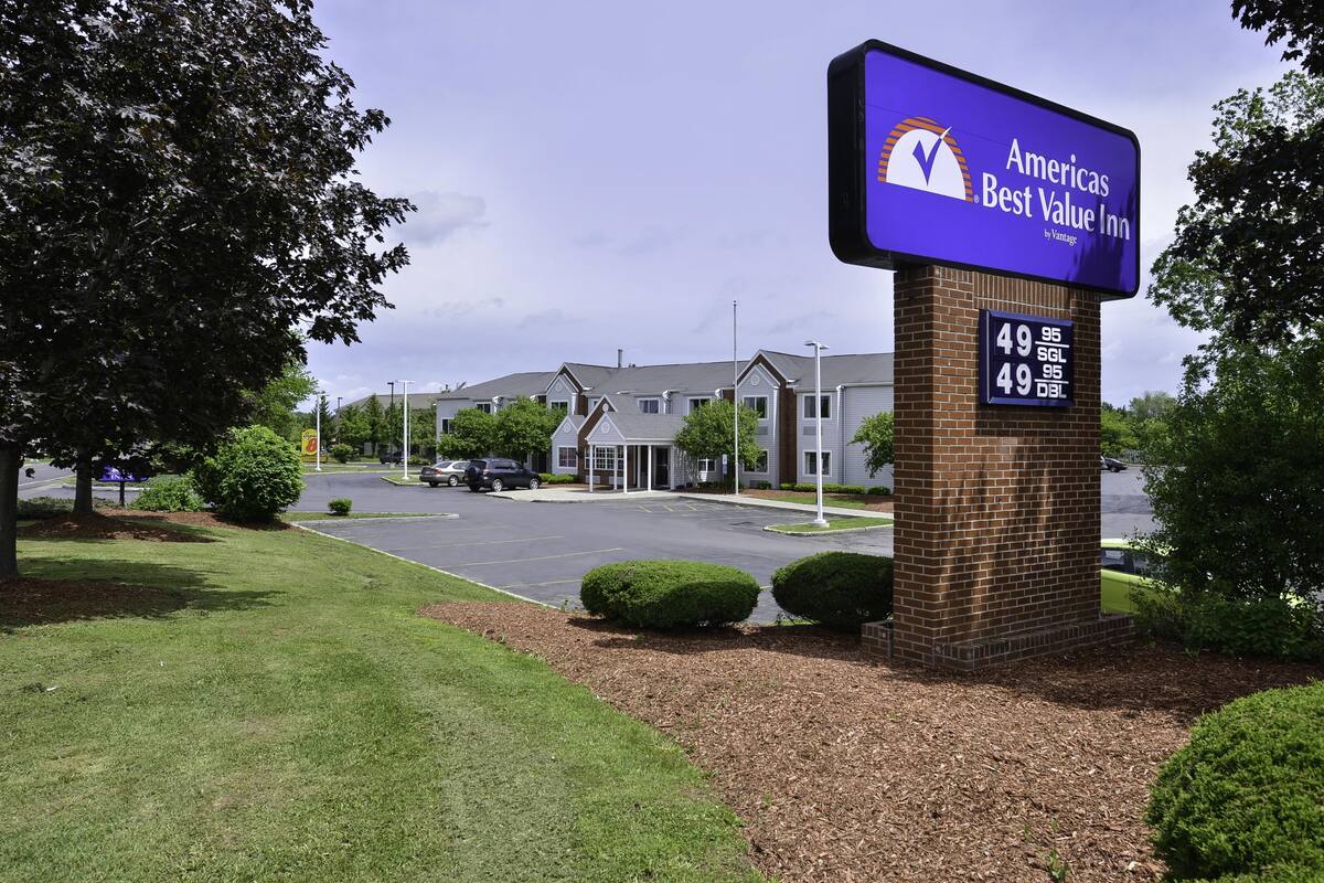A brick pillar with a sign for Ameris Best Value Inn, a parking lot, and a building with a grey roof.