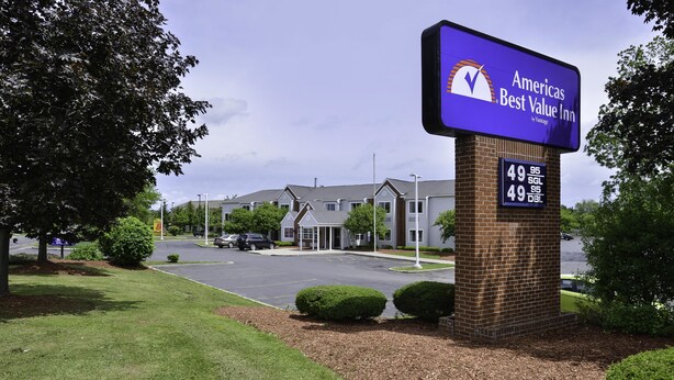 A brick pillar with a sign for Ameris Best Value Inn, a parking lot, and a building with a grey roof.