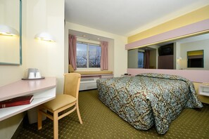 Ein Hotelzimmer mit Bett, Schreibtisch, Stuhl, einem Fenster mit Vorhängen und einem Fernseher auf einem Schrank.