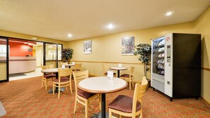 A hotel lobby with round tables and chairs, a vending machine, and a reception desk.