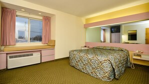 A hotel room with a bed, a window seat, a mirror, and a heater.