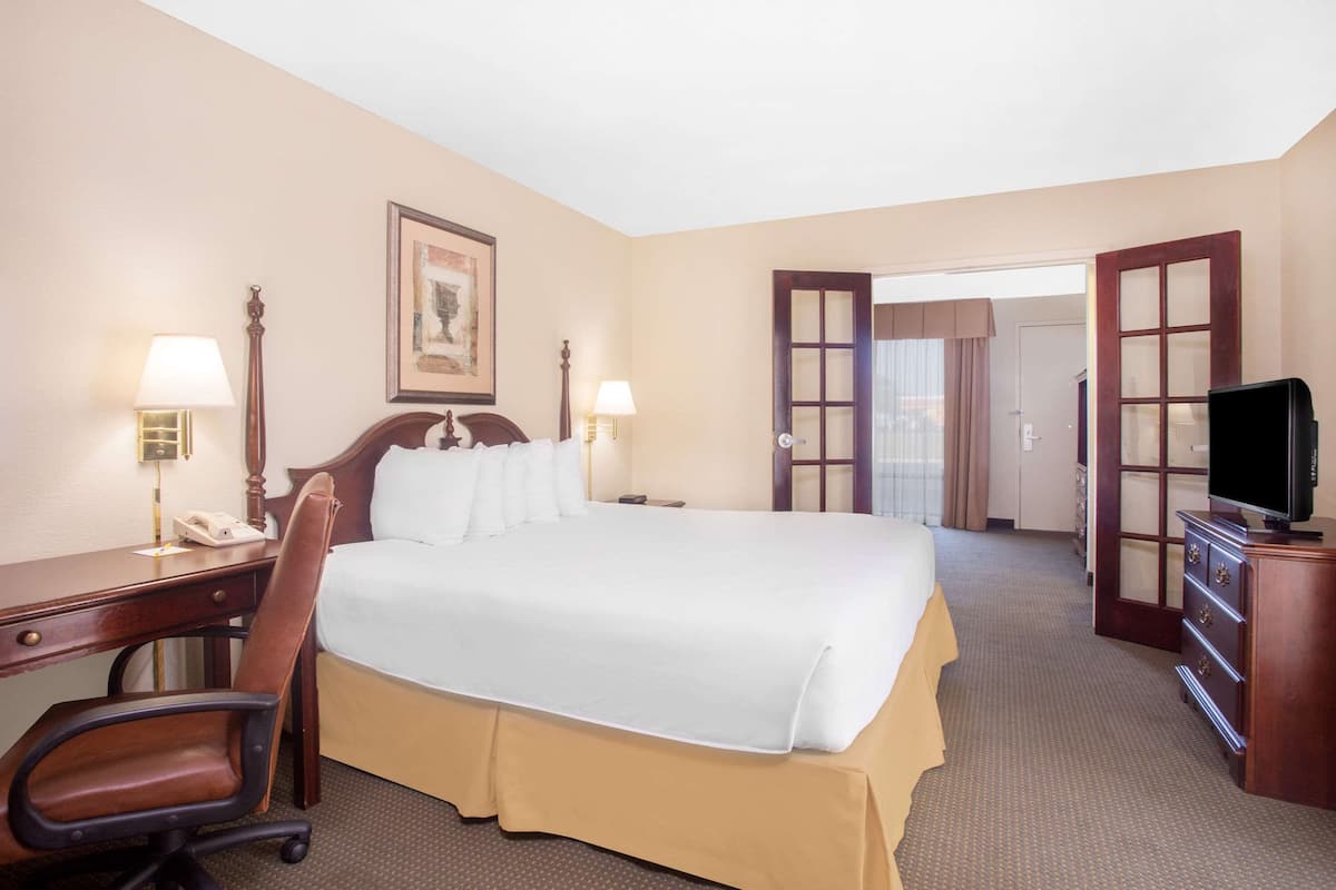 Une chambre d’hôtel avec un grand lit, un bureau avec un téléphone, une chaise, une télévision et une porte donnant sur une autre pièce.