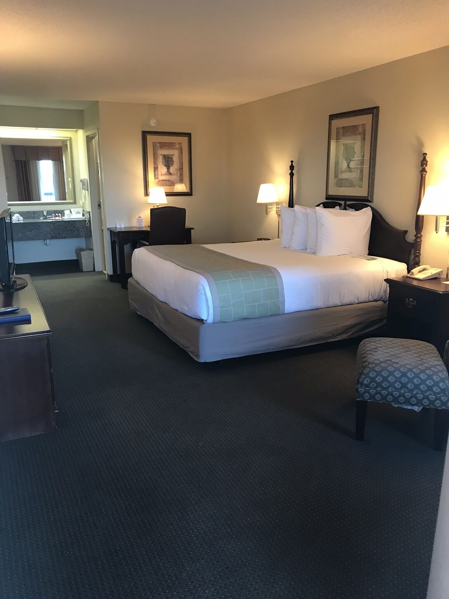 A hotel room with a large bed, two bedside lamps, a desk with a computer, a chair, and a small table.